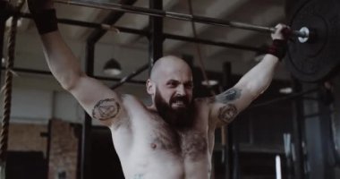 Yakın çekim yavaş çekim. Beyaz bir adam, spor salonunda levyeyi kaldırıyor. Aşırı ağırlık antrenmanı yapıyor..
