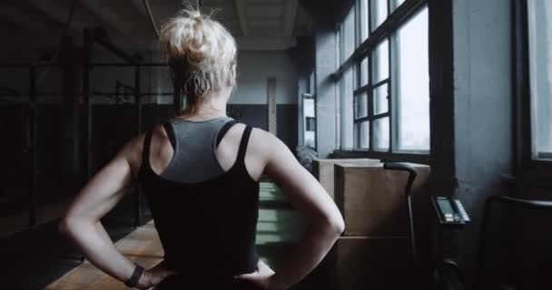 Camera segue la giovane donna bionda atletica che cammina da sola in una grande palestra vuota, preparandosi ad esercitare il rallentatore. — Video Stock