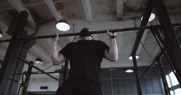 Atlético joven caucásico hombre haciendo ejercicios pull-up durante el entrenamiento funcional en gran gimnasio atmosférico cámara lenta. — Vídeo de stock