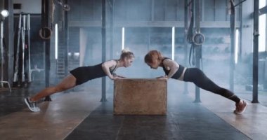 Yan görünüş mutlu çekici sarışın kadın spor salonunda kişisel bayan antrenörle ağır çekimde şınav çekiyor..