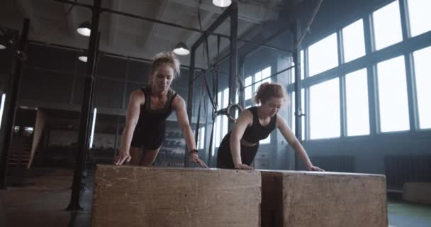 Lambat gerak dua atlet wanita cantik muda bekerja keluar, melakukan push-up dan tepuk tangan bersama-sama di gym atmosfer. — Stok Video