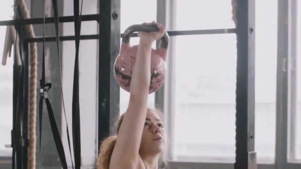 Молодая спортивная рыжеволосая белая женщина, поднимающая тяжелый гири в большом спортзале, замедленная съемка, активный образ жизни — стоковое видео