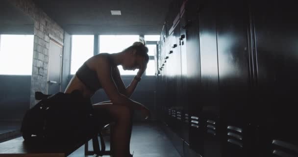 Triste mujer atlética caucásica sentada sola en el vestuario oscuro del gimnasio, sintiéndose perdida y molesta superando el fracaso cámara lenta. — Vídeos de Stock