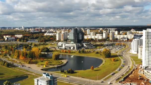 Беспилотник летит назад от здания Национальной библиотеки в Минске к красивому осеннему мегаполису — стоковое видео