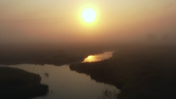 Drönare flyger genom tjock dimma över mystiska fält och slingrande flod, stiger för att avslöja episka stigande sol dal panorama — Stockvideo