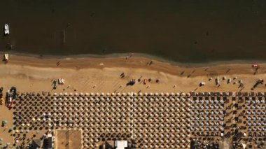 Üst manzara, deniz kıyısında uçan insansız hava aracı, büyük dalga kırıcılara doğru sıralanmış sandalyeli mükemmel kumlu plaj..