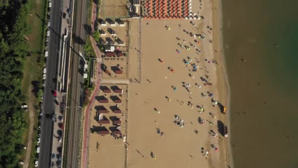 Vista superior de la perfecta costa del mar de verano, sobrevuelo de la playa de arena pública con filas de sillas, sombrillas y ferrocarril. — Vídeos de Stock