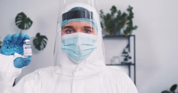 COVID-19 vacina. Médica cientista do laboratório usa terno médico, máscara e escudo segurando frasco de cura contra coronavírus — Vídeo de Stock