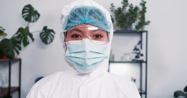 Retrato de feliz jovem médico multicultural vestindo terno médico, máscara e óculos durante a pandemia olha para a câmera — Vídeo de Stock