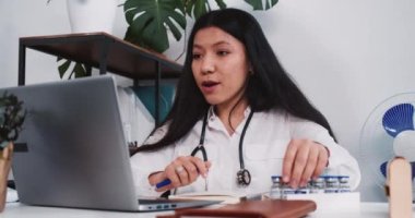 Profesyonel güzel melez doktor kadın dizüstü bilgisayarda uzak bir hastaya aşı tedavisi uyguladığını gösteriyor..