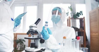 Hastalıkla mücadelede umut. Korunma giysisi içindeki profesyonel kadın doktor klinikteki yeni aşıyla birlikte matarayı tutuyor.