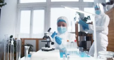 COVID-19 aşısı üretiyor. Tam korumalı iki kadın eczane bilim adamı klinikteki yeni ilaç şişesini test ediyor..