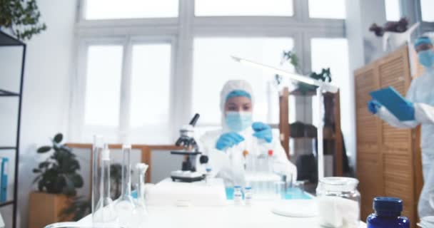 Kémiai labor tudós a munkahelyén. Fiatal, fókuszált gyógyszerészeti szakértő védőöltözet használatával mikroszkóp vizsgálati vakcina. — Stock videók