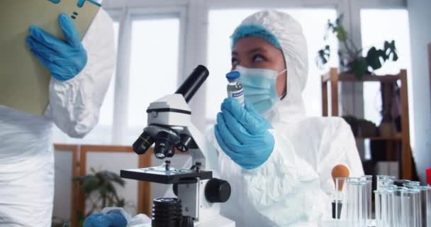 Cientista de laboratório de clínica feminina feliz em terno de proteção e escudo segurando frasco com nova vacina. Esperança no combate à doença — Vídeo de Stock