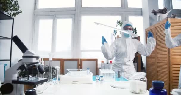 Celebrando el éxito. Dos emocionados y felices doctores de laboratorio químico en trajes de protección bailan cangrejo en el trabajo. — Vídeos de Stock