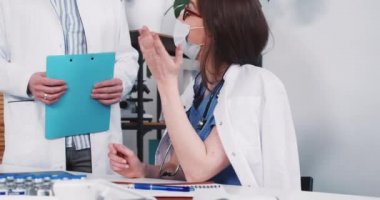 Laboratuvar önlüklü, maske takmış iki beyaz doktor iş yerinde birbirlerine danışıyorlar, açık klinik masasında davayı tartışıyorlar..