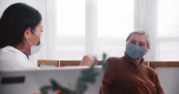 Médica de raça mista em jaleco oferece frasco de medicamento vacinal para mulher cliente sênior caucasiana, ela concorda em. — Vídeo de Stock