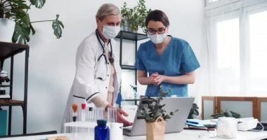 Takım çalışması konsepti. Mavi önlüklü genç beyaz hemşire dizüstü bilgisayara bakar, laboratuvar önlüklü kıdemli doktorla konuşur..