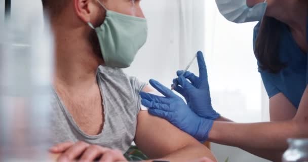 Yakın plan aşı konsepti. Mavi önlüklü hemşire erkek hastaya aşı iğnesi yapmak için şırınga kullanıyor.. — Stok video