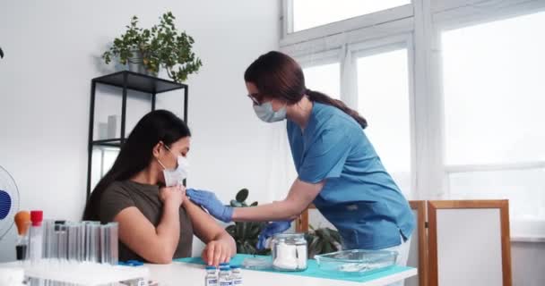 Vaccinatie concept. Jonge blanke medische verpleegkundige vrouw in blauwe scrubs geeft injectie schot aan gemengde ras patiënt. — Stockvideo