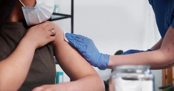 Close-up verpleegkundige in blauwe scrubs, medische handschoenen geeft vaccin injectie schot met hypodermale naald aan jonge vrouwelijke cliënt — Stockvideo