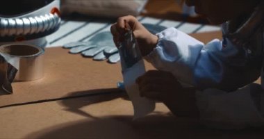 Sinematik yakın çekim, uzay pilotu oynayan çocuk elleri, gümüş selobant ile karton parçaları yapıştırırken eğlenmek..