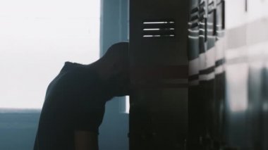 Genç atletik adamın silueti, karanlık soyunma odasında tek başına üstünü değiştiriyor. Yarışmalarda başarısız olduktan sonra stresin üstesinden geliyor..