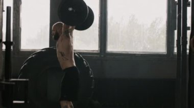 Geniş açıda, beyaz tenli aşırı halterci bir sporcunun, ağır halterlerle spor salonundaki büyük spor salonunda çalışması.