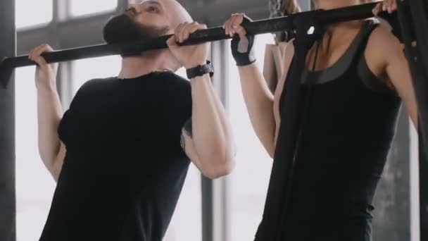 Close-up young happy fit Caucasian man and woman doing chin-ups together. Exercising with personal fitness coach. — Stock Video