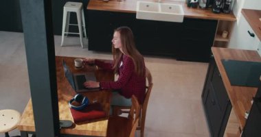 Kafkasyalı güzel, mutlu, bağımsız bir kadının evde çalışmak için bilgisayarını kullanıp kahve yudumladığı yüksek açılı bir çekim..