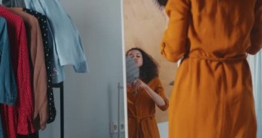 Kıvırcık saçlı, dans eden, giyinme odasındaki aynada şık bir şapka takmaya çalışan mutlu, heyecanlı, genç, heyecanlı bir yarış blogcusu kadın..