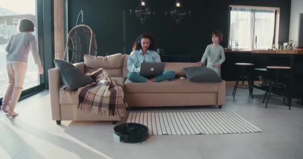 Két zajos tinédzser gyerek rohangál fáradt, stresszes egyedülálló anya próbál távolról dolgozni laptoppal otthon a kanapén. — Stock videók