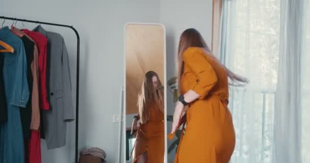Visão traseira jovem bonita animado caucasiano moda blogger mulher dançando no espelho ao tentar várias roupas e chapéu — Vídeo de Stock