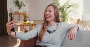 Web konferans uygulaması. Çevrimiçi arkadaşlarıyla konuşmak için akıllı telefon görüntülerini kullanan neşeli sarışın kadın gülümsüyor..