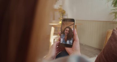 Web konferansı konsepti. Omuz hizasında, sarışın kadın açık evdeki akıllı telefon ekranından melez ırk arkadaşıyla konuşuyor..