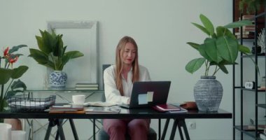 Güzel, ciddi, başarılı, sarışın patron iş kadını, modern ışık ofis masasında dizüstü bilgisayar kullanarak tek başına çalışıyor..