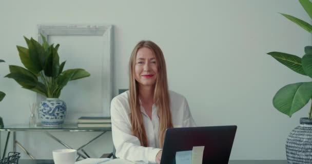 Semmi stressz a munkahelyen. Közelíts rá a boldog, gyönyörű 30-as évekbeli üzletasszony dolgozik a modern irodában laptoppal, mosolyogva a kamerába. — Stock videók