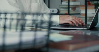 Beyaz gömlekli, mutlu ve zarif iş kadınının yakın çekim elleri dizüstü bilgisayar kullanır, modern ofis masasında notlar alır..