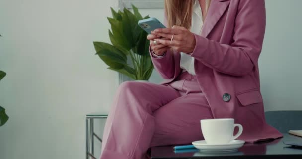 Skjuter bara en gång. Närbild elegant affärskvinna i rosa kostym med hjälp av smart telefon app, med kaffe vid lätt kontorsbord — Stockvideo