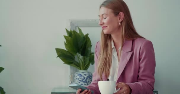 Leven en balans op het werk. Gelukkig mooi elegant zakenvrouw met behulp van smart phone, nippen koffie aan licht kantoor tafel. — Stockvideo