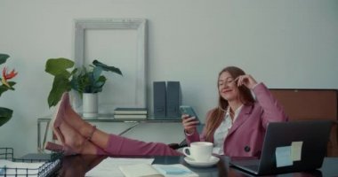 Mutlu başarılı, güzel bayan patron ofis masasında gülümseyen cep telefonu uygulamasını kullanarak internetten bir şeyler alıyor..