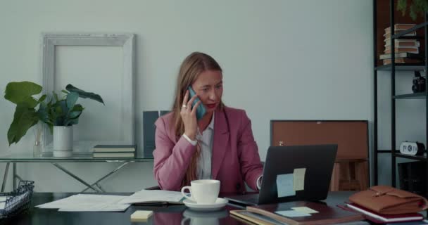 Estoy ocupado en el trabajo. Hermosa mujer de negocios relajada habla por teléfono, trabaja con el ordenador portátil, toma notas en la mesa de oficina moderna. — Vídeos de Stock