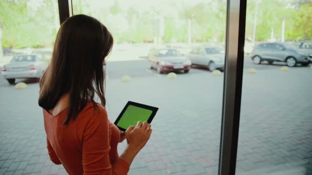 Женщина стоит у окна и работает на планшете. зеленый экран — стоковое видео