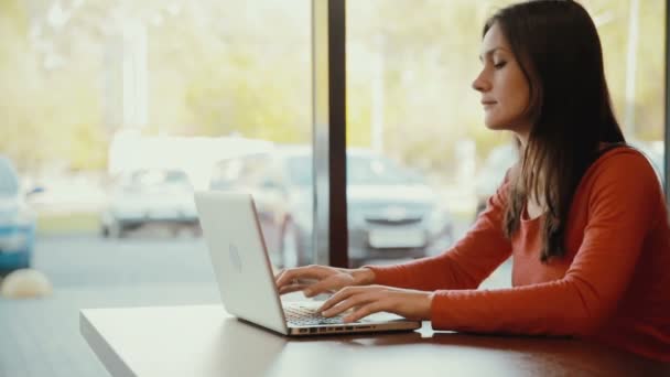 Женщина печатает на ноутбуке и улыбается в кафе — стоковое видео