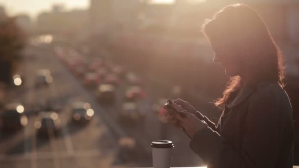 Schönes Mädchen benutzt ein Smartphone auf einer Stadtbrücke — Stockvideo