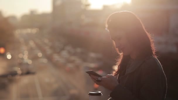 Hermosa chica utiliza un teléfono inteligente en un puente de la ciudad — Vídeos de Stock