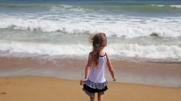 小さな女の子がビーチで波と遊んで — ストック動画