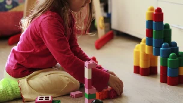 Милая маленькая девочка играет с игрушечными блоками дома — стоковое видео