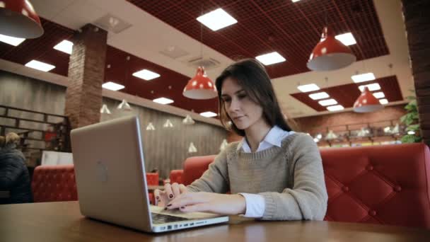 Mujer trabajando en la computadora portátil moderna en la cafetería — Vídeos de Stock