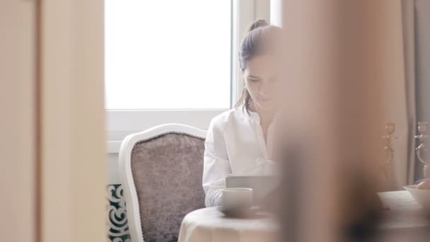 Γυναίκα χρησιμοποιώντας δισκίο και πίνοντας τον καφέ από πίνακα — Αρχείο Βίντεο